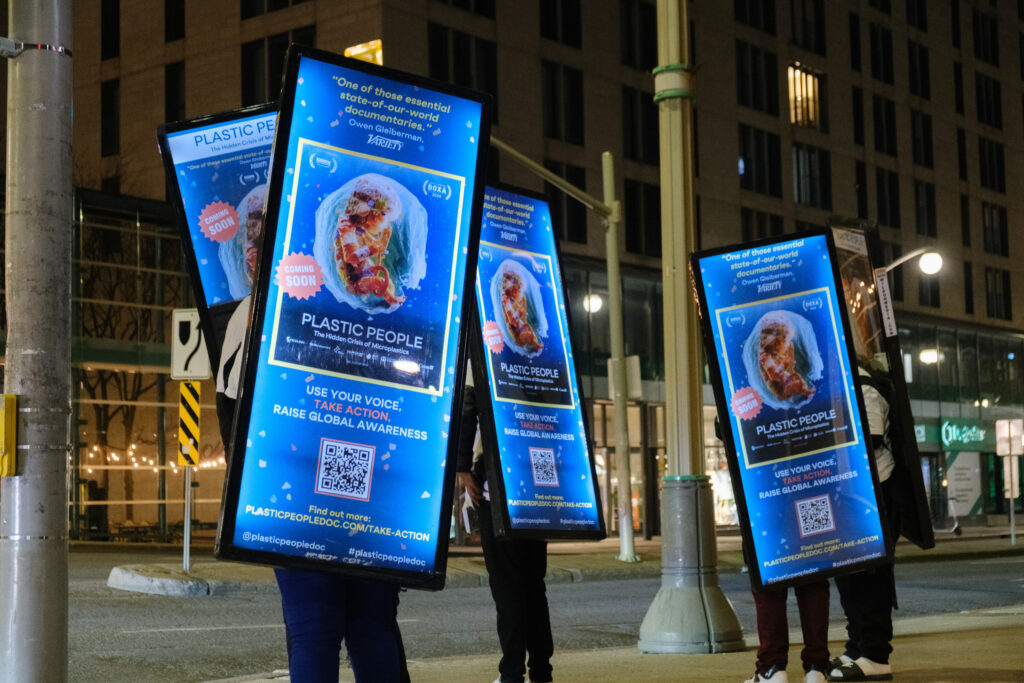 Plastic People walking billboard posters at night.