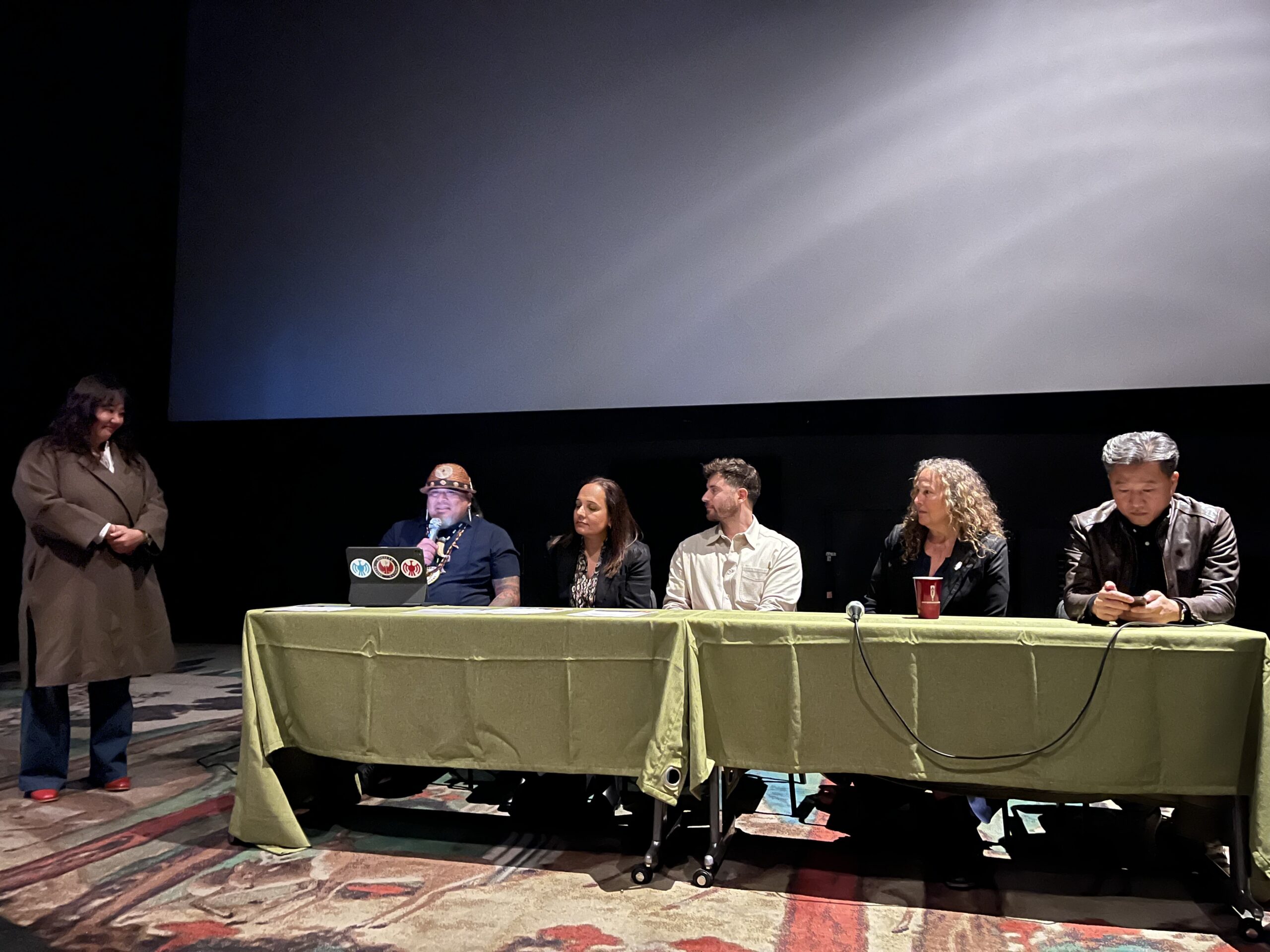 Five people sitting at a table and one woman standing beside it. Panel is discussing the film Plastic People.